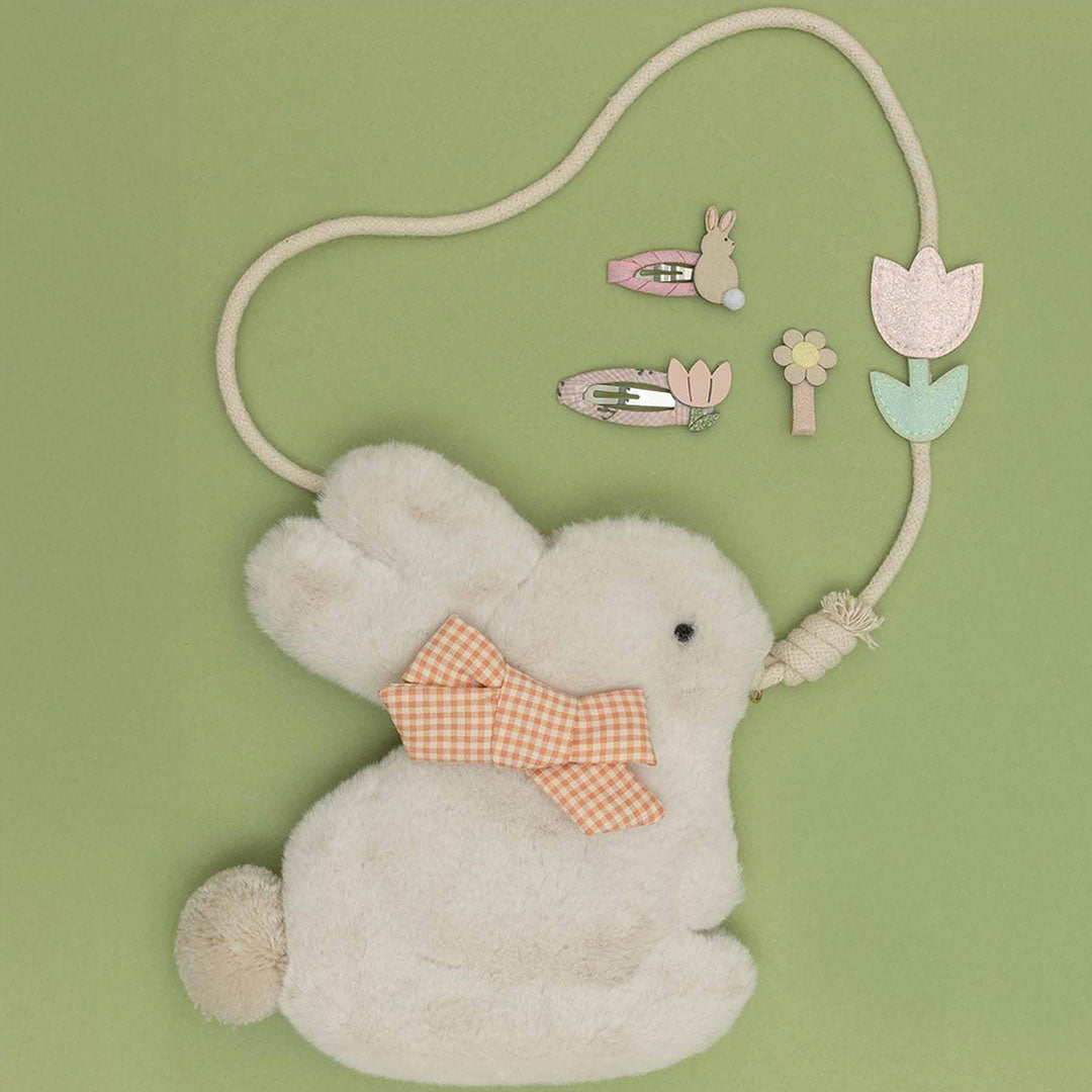 Het mimi & lula fluffy konijnen schoudertasje ligt op een groene achtergrond met bijpassende haarclips in de vorm van een konijn en tulpen.