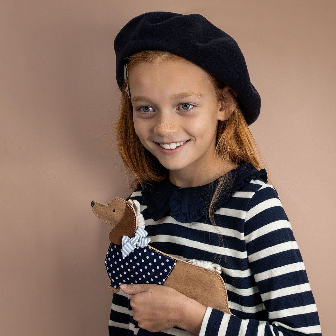 Een lachend meisje met een baret en gestreepte trui houdt het mimi & lula teckel schoudertasje vast.