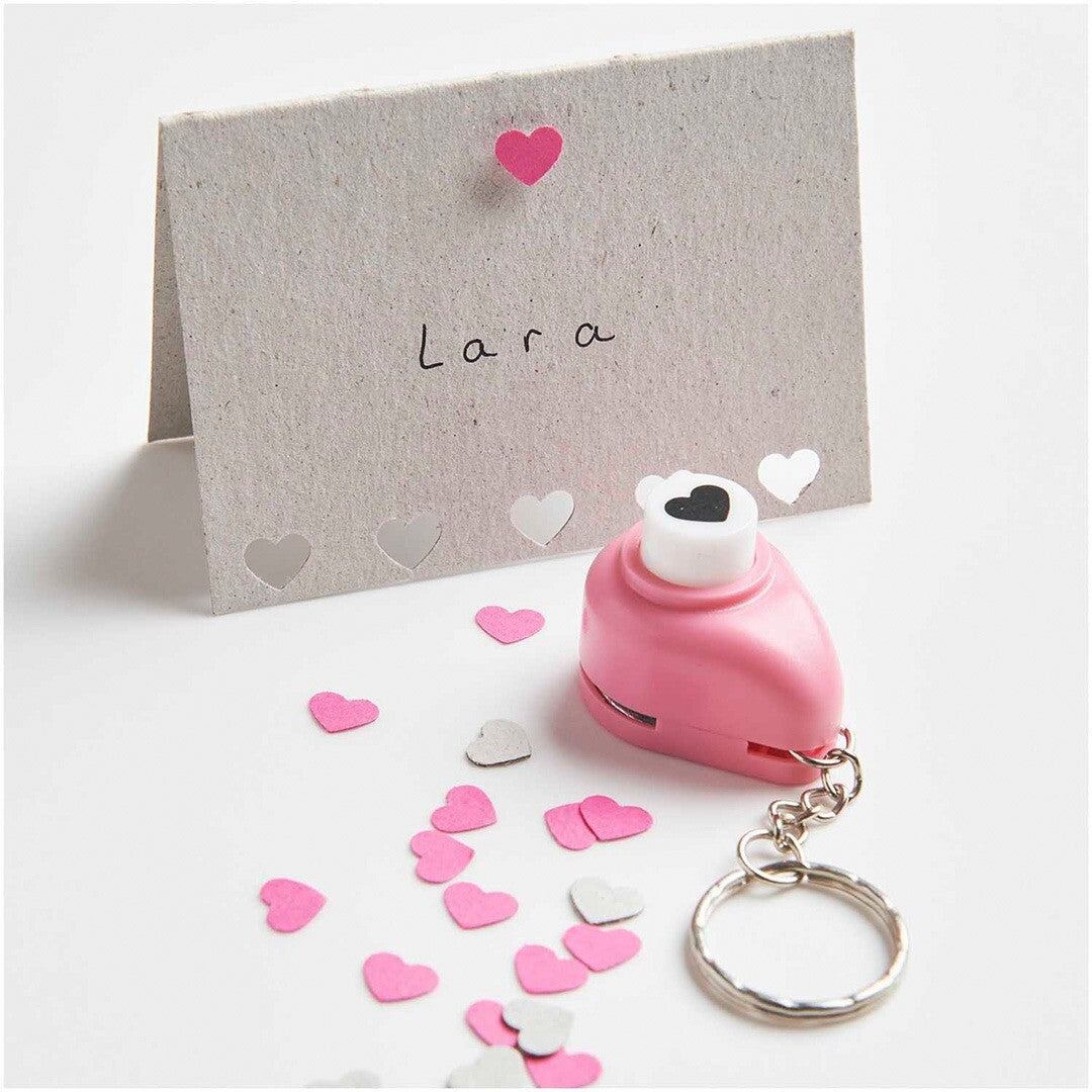 Roze mini perforator sleutelhanger op een tafel met geponste hartjes en een kaartje met de naam Lara.