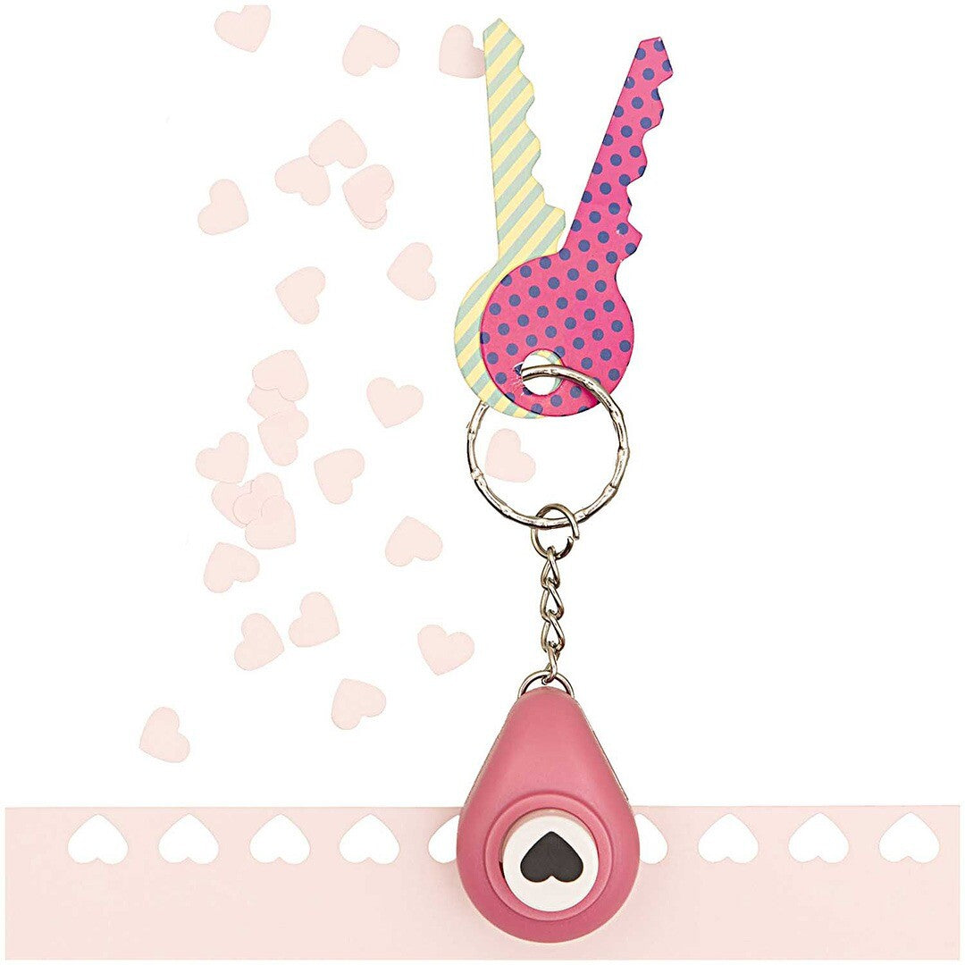 Roze mini perforator sleutelhanger met twee decoratieve sleutels, hangend boven een strook papier met geponste hartjes.