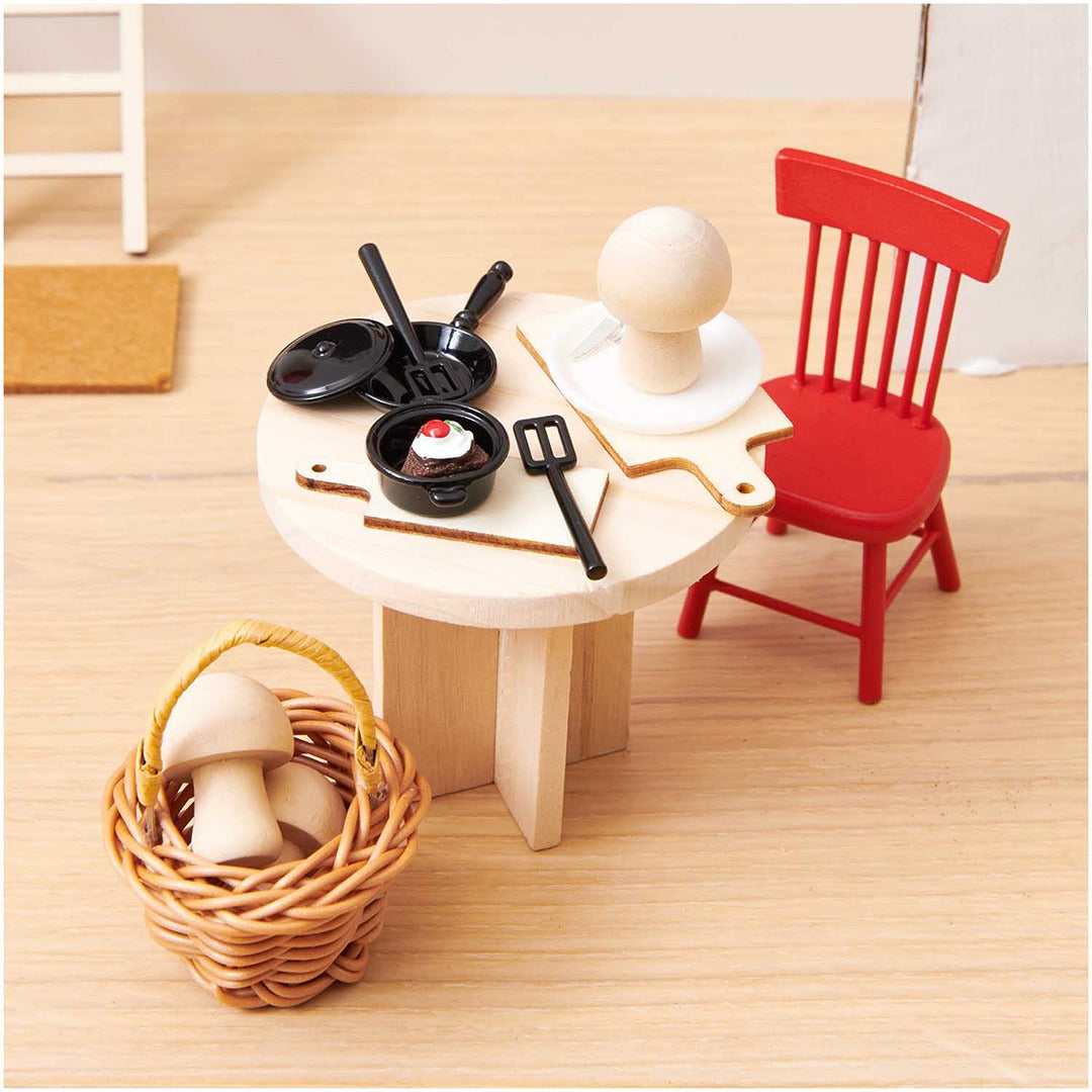 Rode houten miniatuurstoel aan een tafel met poppenhuis kookaccessoires en een mandje met paddenstoelen.