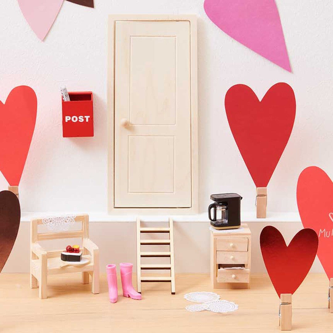 Een collectie poppenhuis accessoires, waaronder de miniatuur koffiemachine, meubels en een deur, op een witte achtergrond met rode harten.