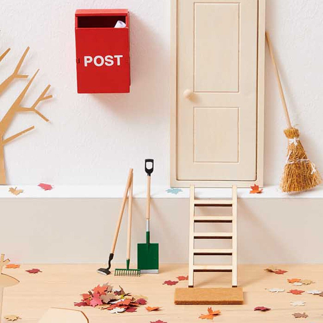 Een Rico Design miniatuur schep en hark staan in een herfstachtige poppenhuissetting met een deur en brievenbus.