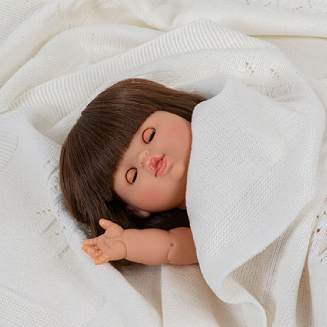 Slapende babypop met bruin haar, gewikkeld in een witte deken.