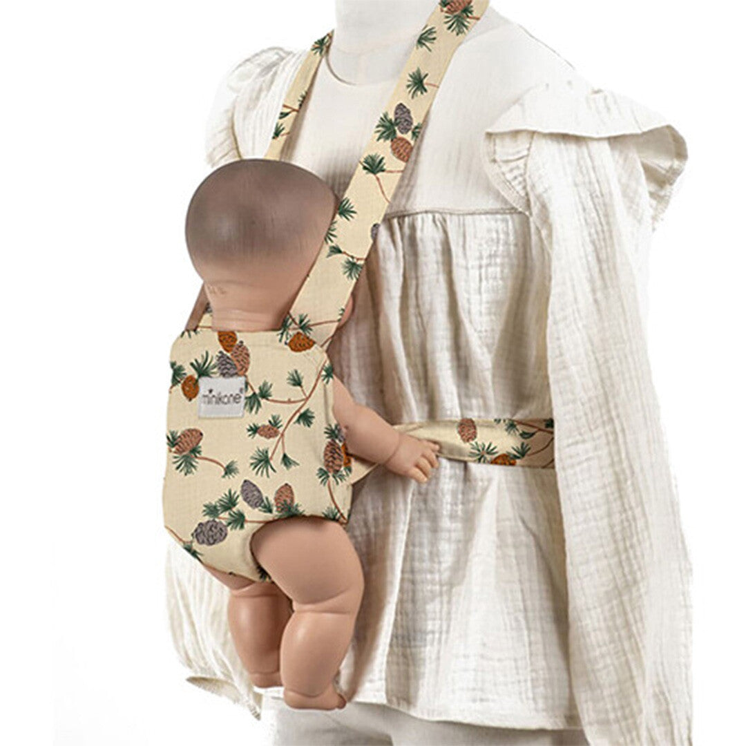 Minikane poppendraagzak met dennenappelpatroon gedragen door een kind met een pop erin.