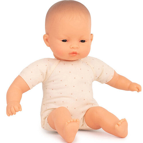 Miniland babypop met Aziatische kenmerken, zittend in een beige rompertje met stippen.