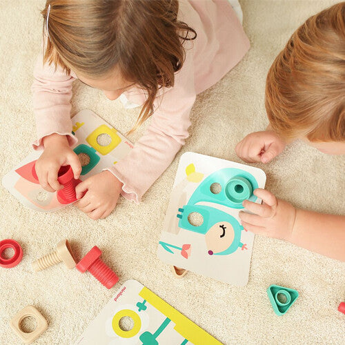 Bovenaanzicht van twee kinderen die op de grond spelen met de veelkleurige bouten, moeren en kaarten met figuren.