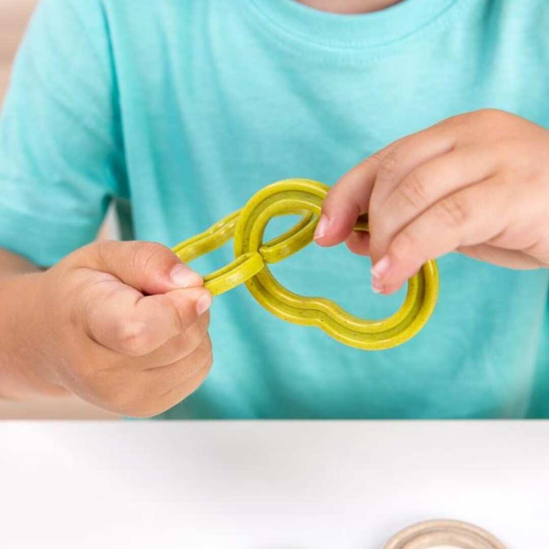 Kinderhanden van een peuter verbinden twee gele plastic schakels van de Miniland bouwset.