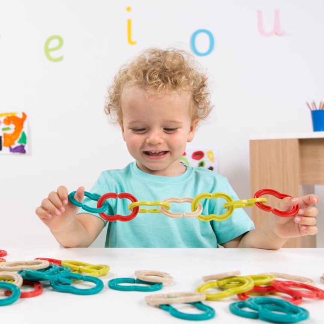 Een lachende peuter speelt met een lange ketting van kleurrijke plastic schakels van de Miniland bouwset.