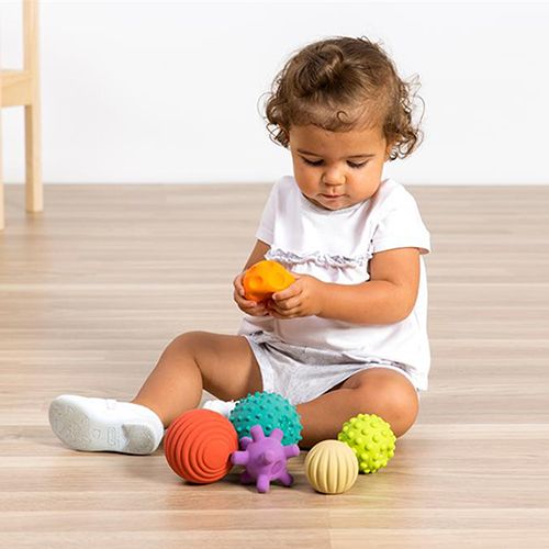 Een baby zit op de vloer en speelt met een oranje miniland sensorische bal, omringd door andere gekleurde ballen.