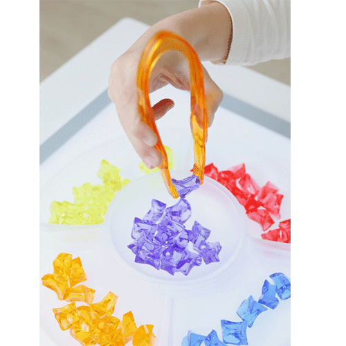 Een hand pakt met een oranje tang een paarse transparante edelsteen uit een sorteerbak.