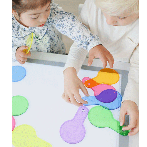 Twee kinderen spelen samen met diverse transparante kleurpaletten op een witte tafel.