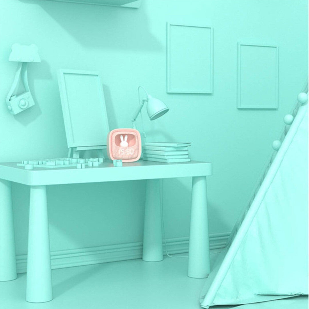 De roze mob wekker en nachtlampje op een tafel in een lichtblauwe kinderkamer.