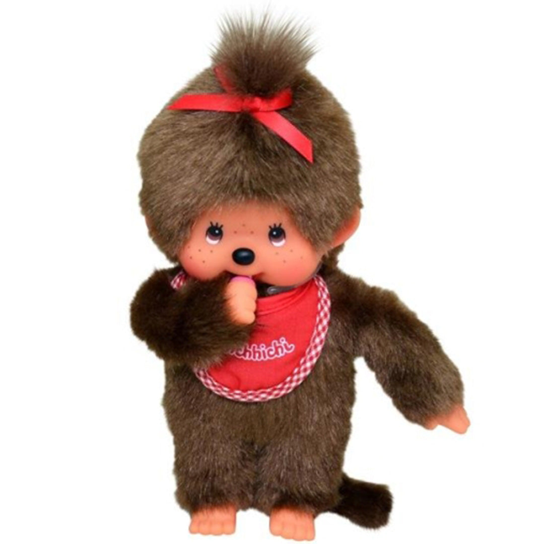 Monchhichi pop jongen met bruine vacht, rode geruite slab en rode strik op het hoofd, met de duim in de mond.