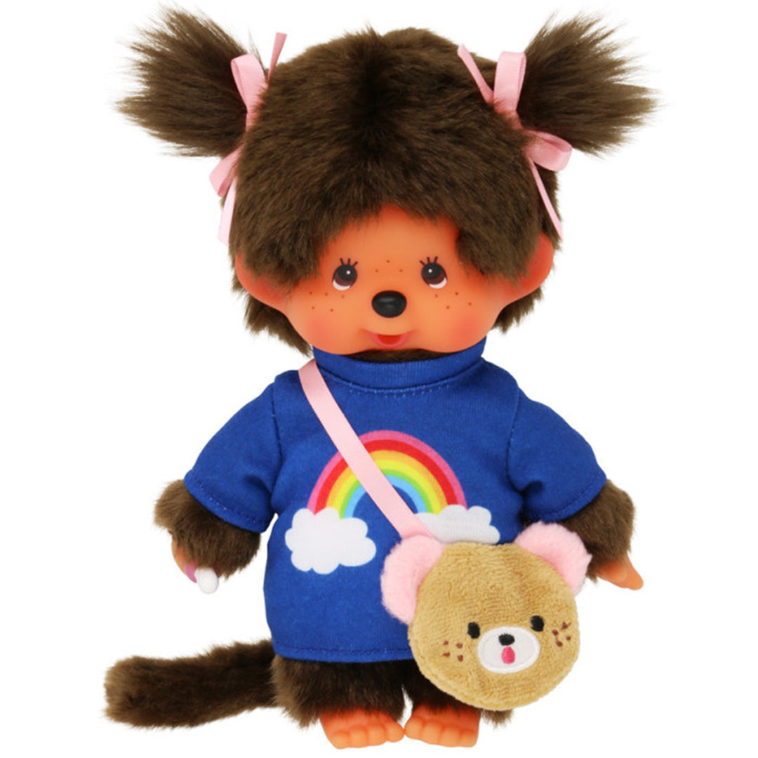 Monchhichi meisje pop met bruine vacht, roze strikjes, een blauw shirt met regenboog en een tasje.