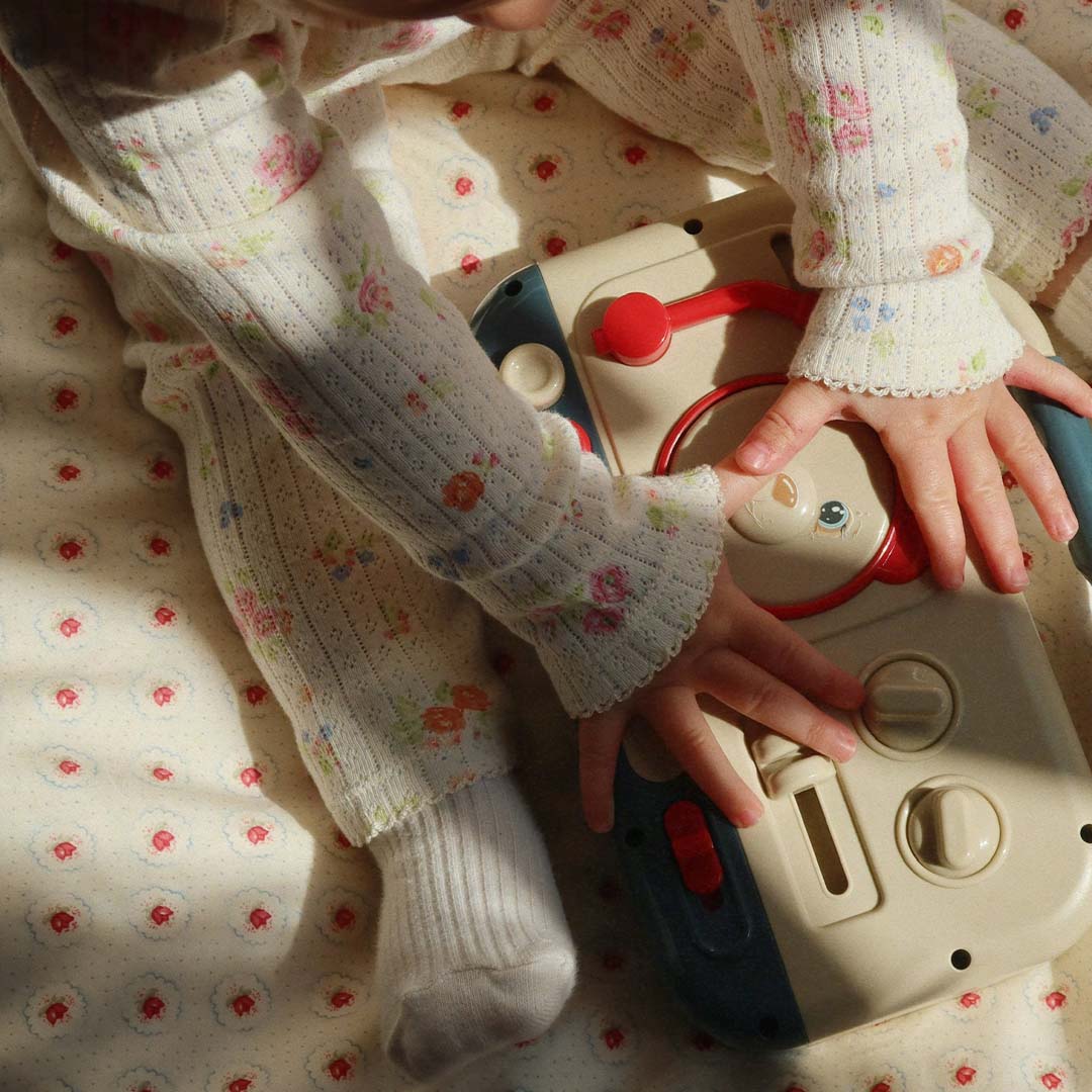 Babyhandjes en -beentjes in een bloemenpakje spelen met de achterkant van het Konges Sløjd muziekspeelgoed.
