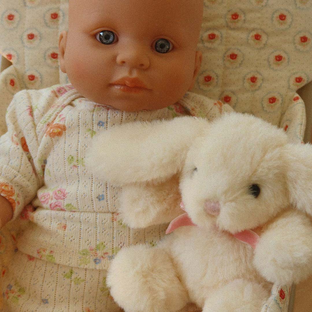 Close-up van de babypop Nonoka in gebloemde kleding met het pluche konijn ernaast.