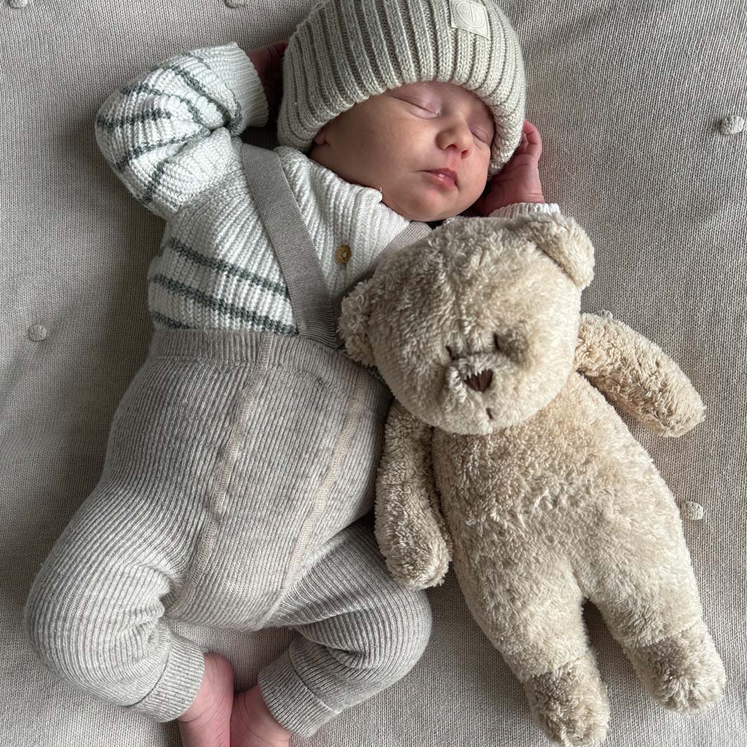 Slapende baby met een Moonie pluchen knuffelbeer op een lichte ondergrond.