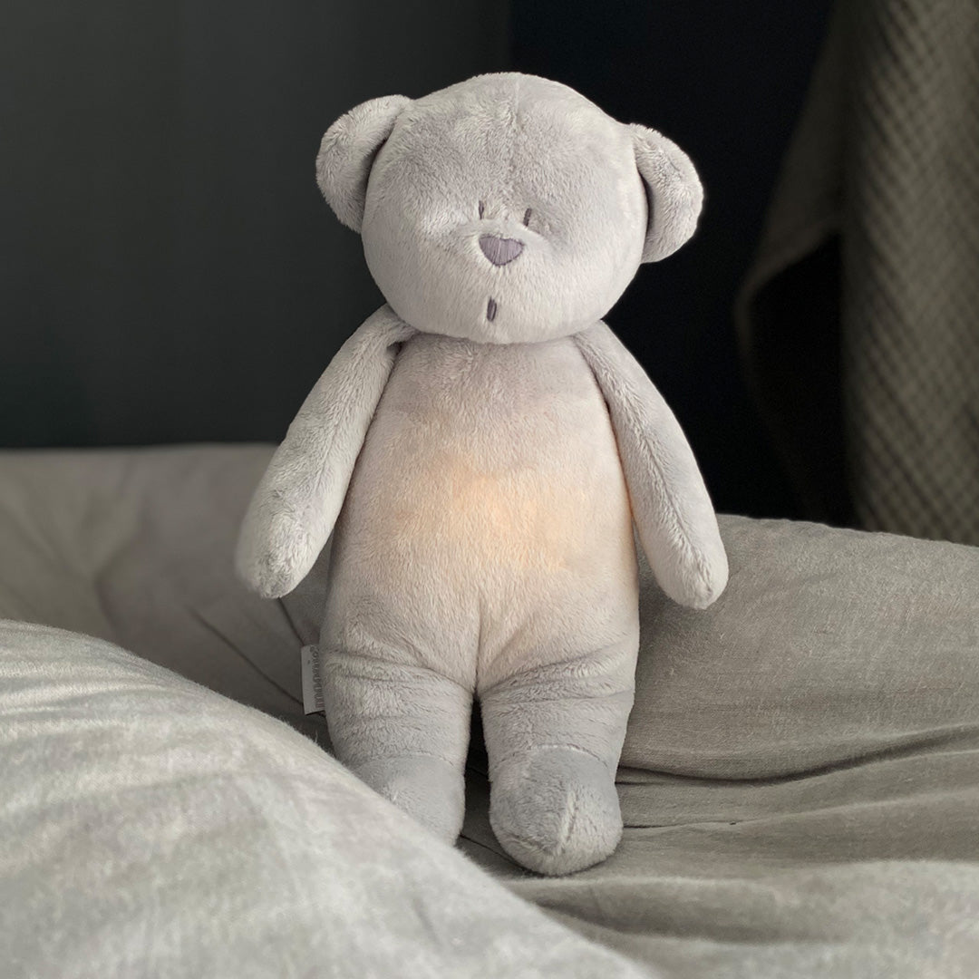 moonie grijze knuffelbeer met oplichtende buik op een bed.