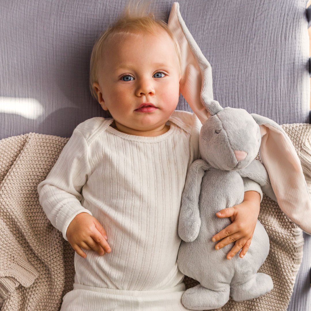 Een baby ligt op een deken en knuffelt het moonie pluchen konijn.