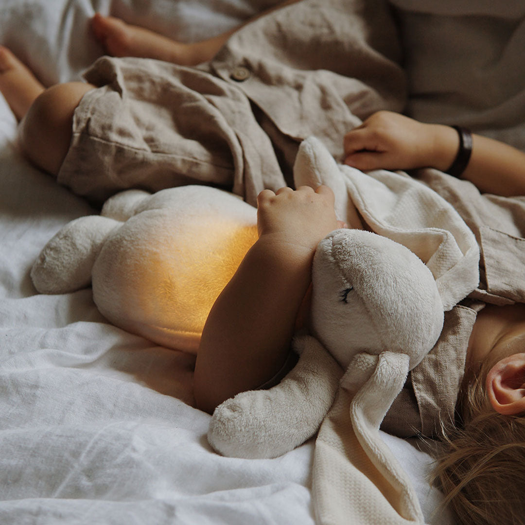 Een kind slaapt met het moonie knuffelkonijn met nachtlamp, dat zachtjes gloeit in bed.