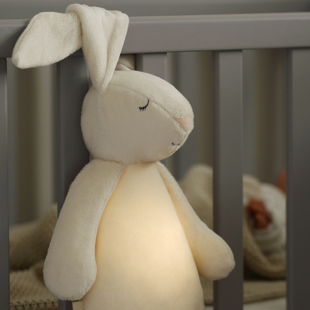 Het moonie knuffelkonijn met nachtlamp hangt aan de spijlen van een wieg en gloeit zachtjes.