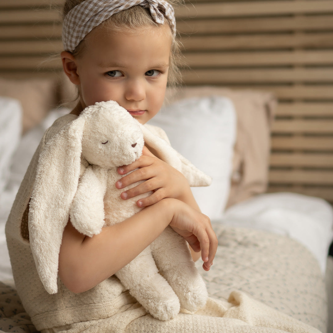 Een meisje zit op bed en knuffelt het Moonie pluchen konijn.