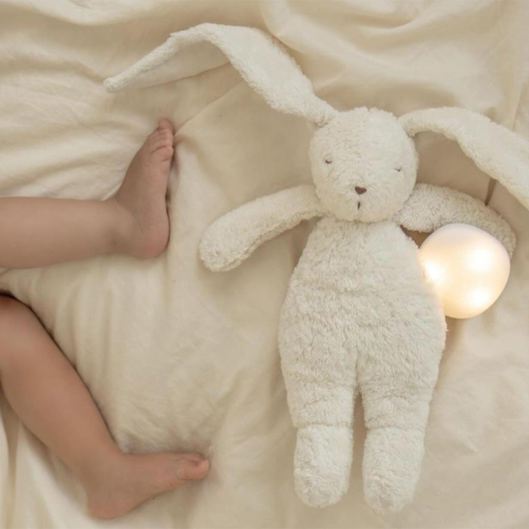 Babyvoetjes liggen naast het Moonie pluchen konijn en een losse ronde lichtbron.
