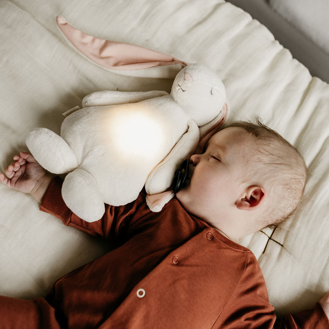 Een slapende baby met een speen, naast het Moonie knuffelkonijn met nachtlamp dat zachtjes gloeit.
