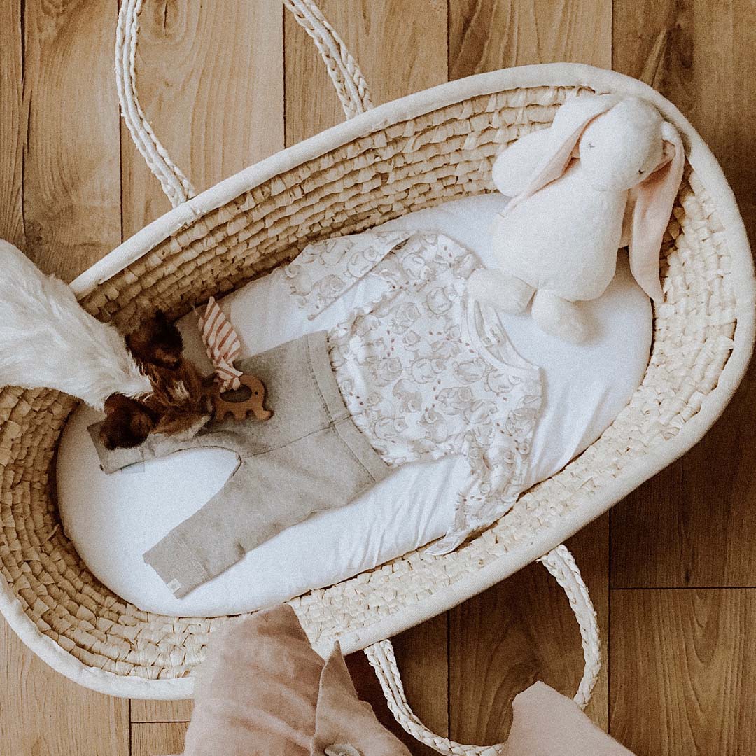 Een rieten Mozesmand met babykleding, een houten speeltje en het Moonie knuffelkonijn.