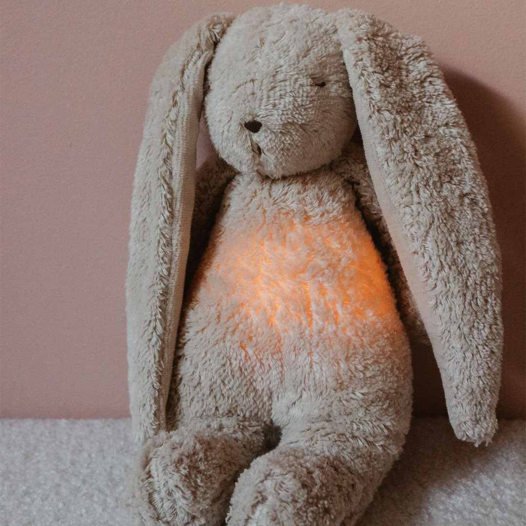 Moonie knuffelkonijn met nachtlampje zit tegen een roze muur.