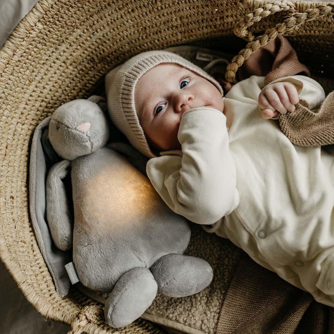 Baby ligt in een rieten mand naast het moonie knuffelkonijn met lichtgevende buik.