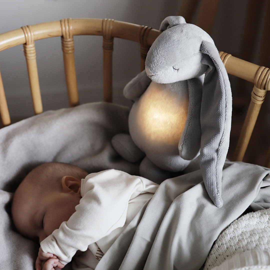 Slapende baby in een wieg naast het moonie knuffelkonijn met lichtgevende buik.