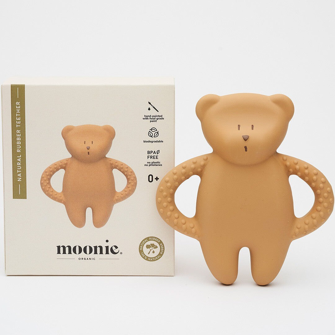 De moonie rubberen bijtring in de vorm van een beige beer ligt naast de productverpakking.