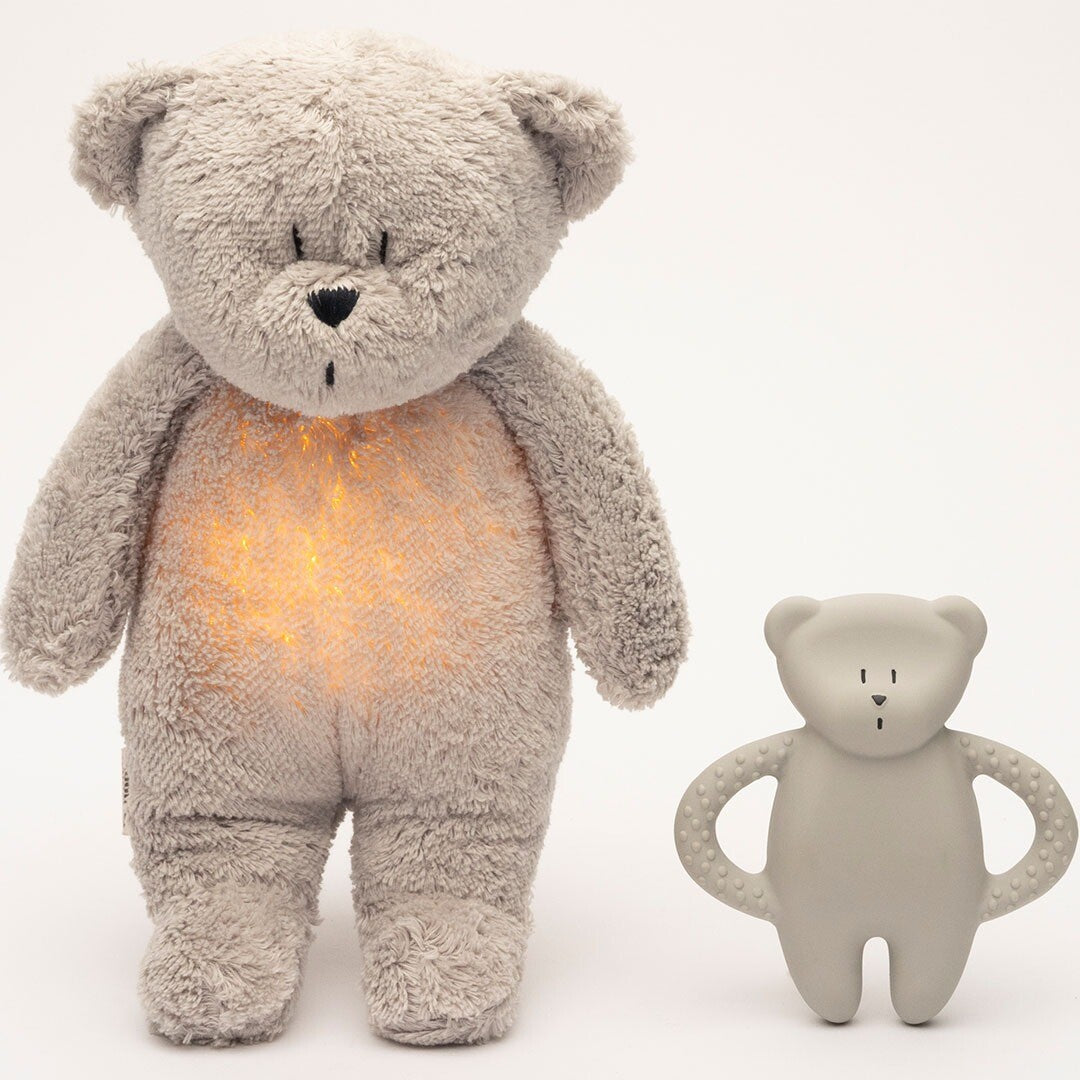 Een grote pluchen beer met lichtgevende buik staat naast een kleine grijze moonie rubberen bijtring in de vorm van een beer.