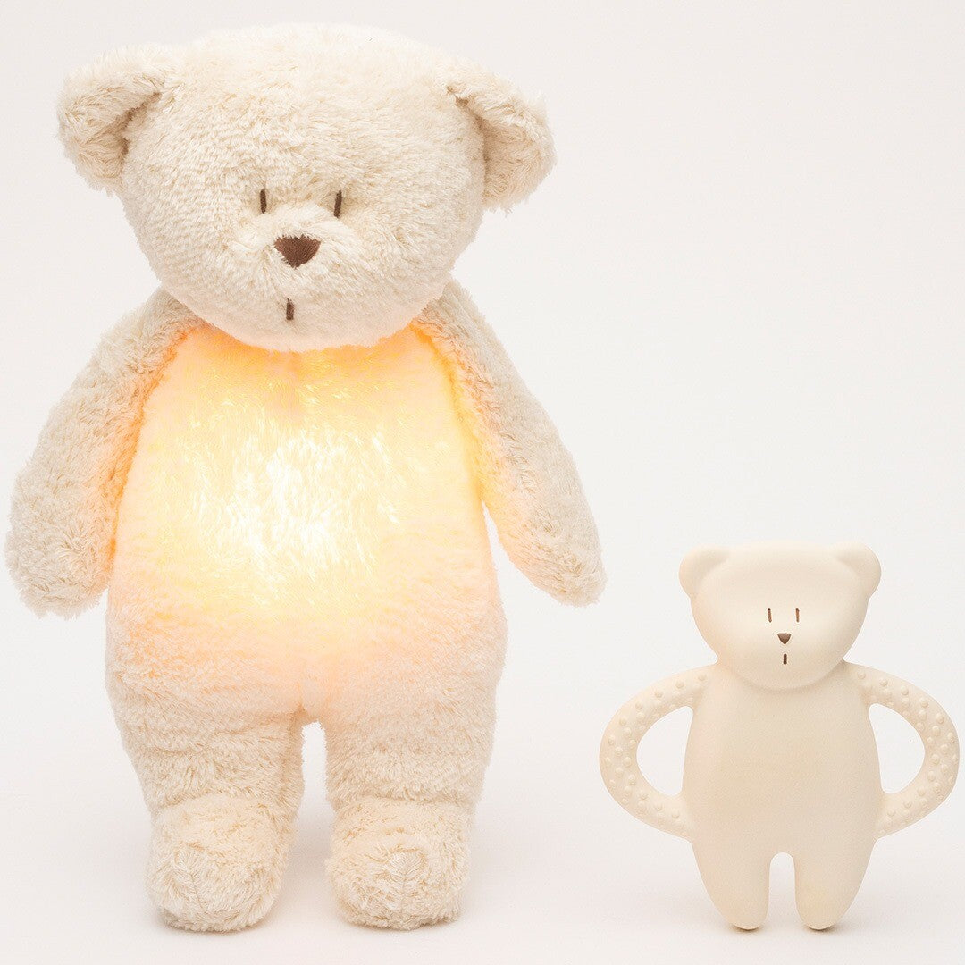 Een moonie bijtring in de vorm van een beige beer staat naast een grote, lichtgevende knuffelbeer.