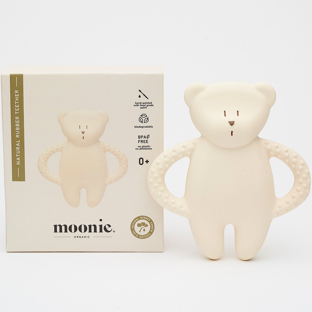 De moonie bijtring in de vorm van een beige beer ligt naast de productverpakking.