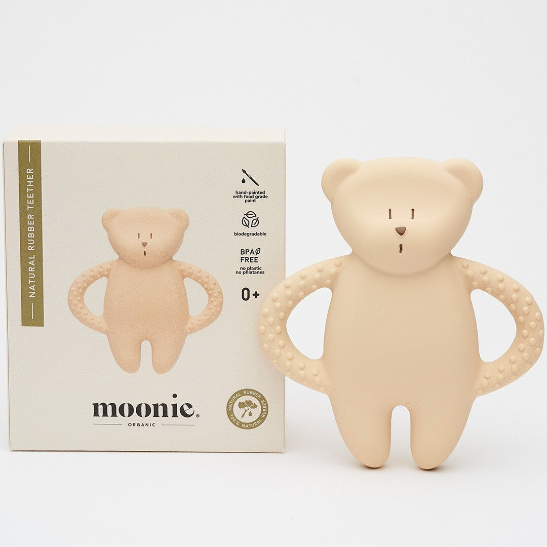De moonie bijtring in de vorm van een beige beer staat naast de witte productverpakking.