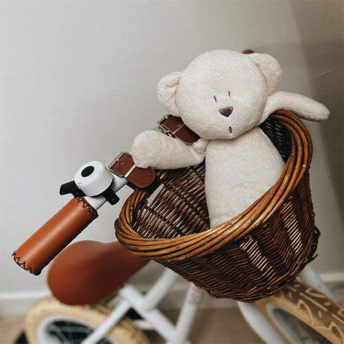 Moonie knuffelbeer met nachtlamp en geluid zit in een rieten mandje op een loopfiets.