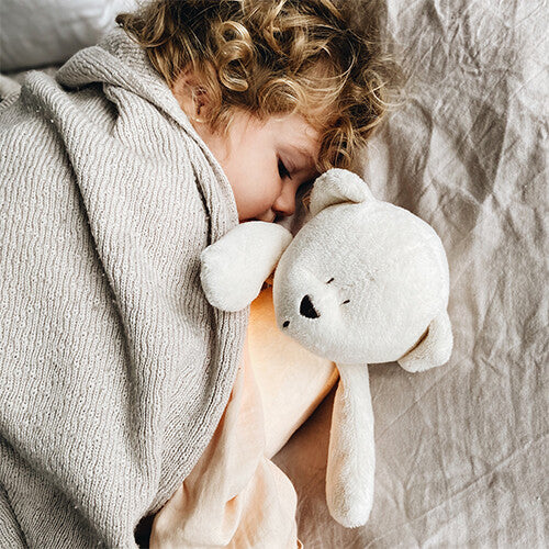 Een slapend kind knuffelt de moonie knuffelbeer met nachtlamp en geluid.