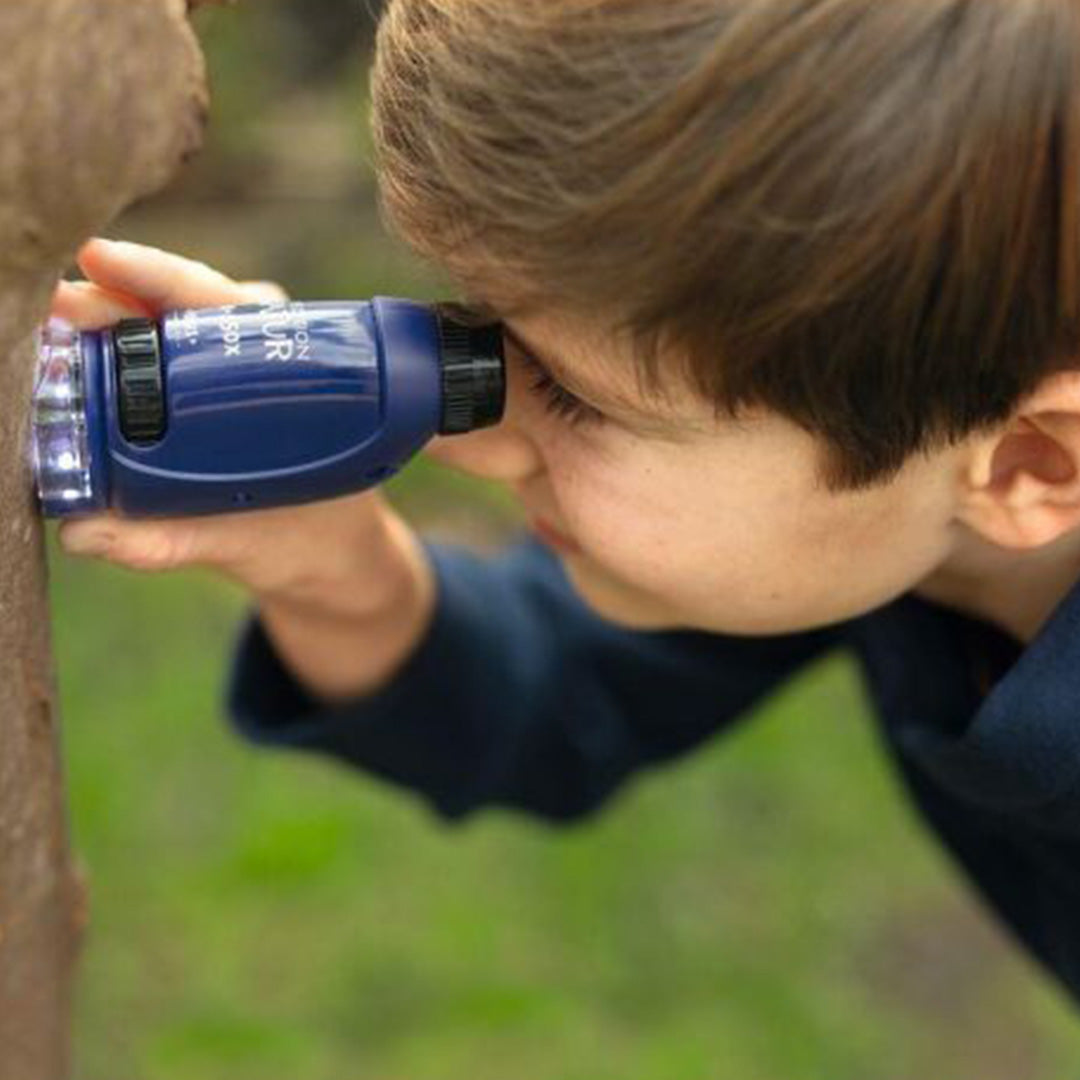 Een kind bekijkt met de blauwe moses. zakmicroscoop een boomstam.