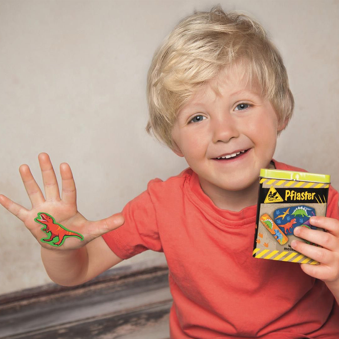 Lachende jongen met een moses. dinosauruspleister op zijn hand en de verpakking in zijn andere hand.