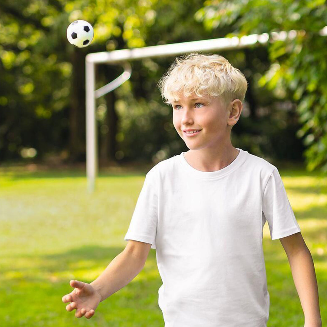 Een jongen speelt buiten met een kleine voetbal stuiterbal.