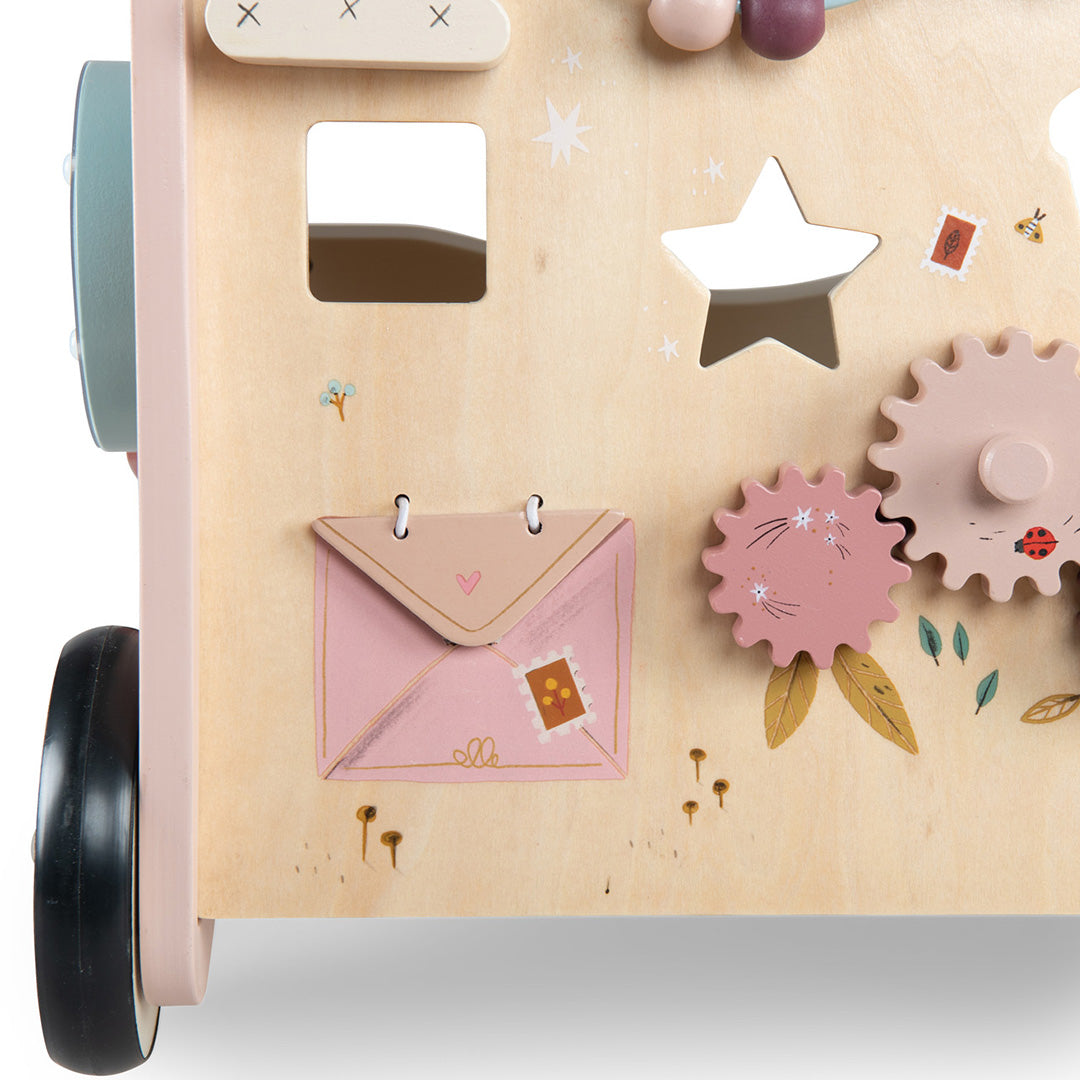 Detail van de houten activiteiten loopwagen met een roze envelop, vormpjes en draaiende tandwielen.