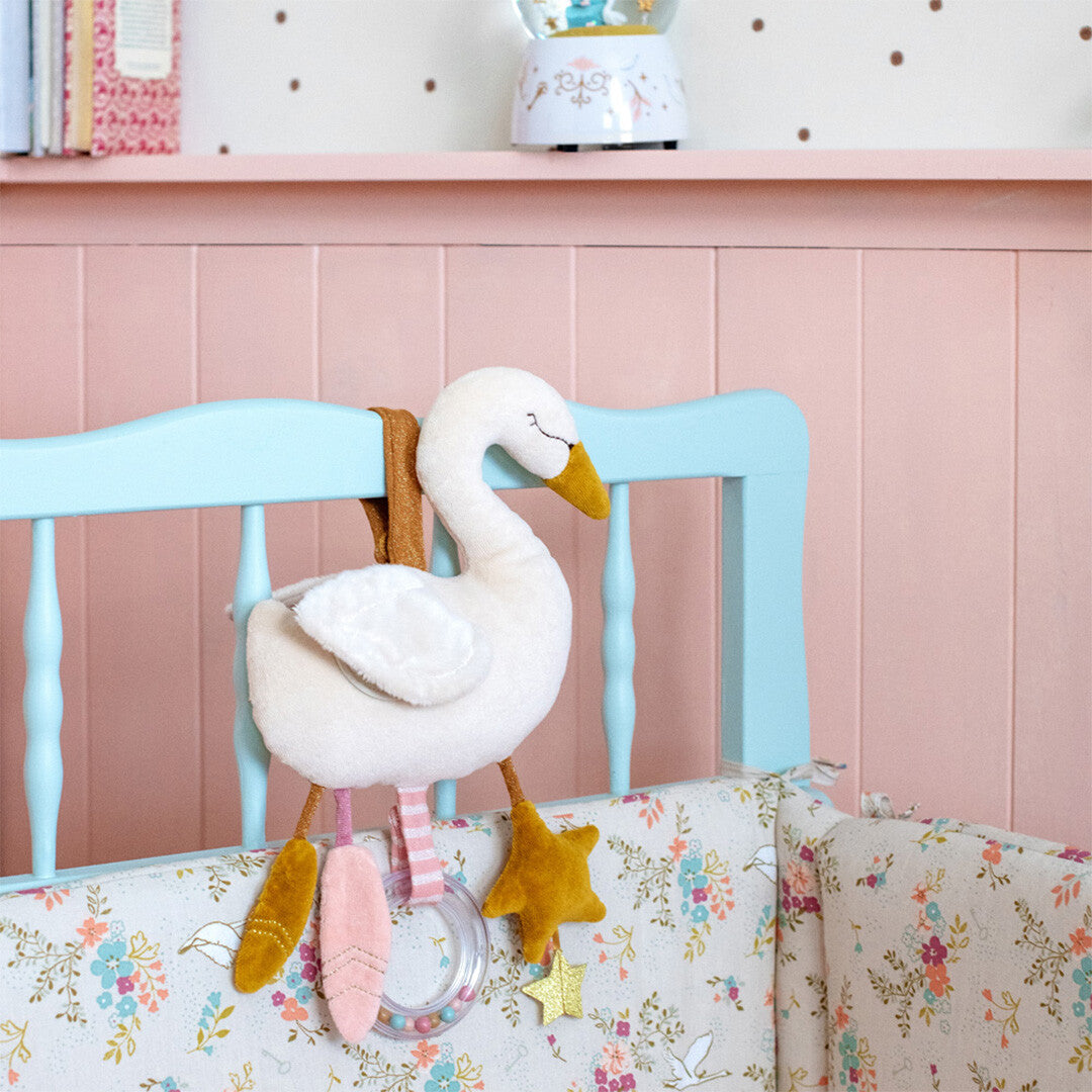De zwaan activiteitenknuffel hangt aan een lichtblauwe babywieg met bloemenpatroon.
