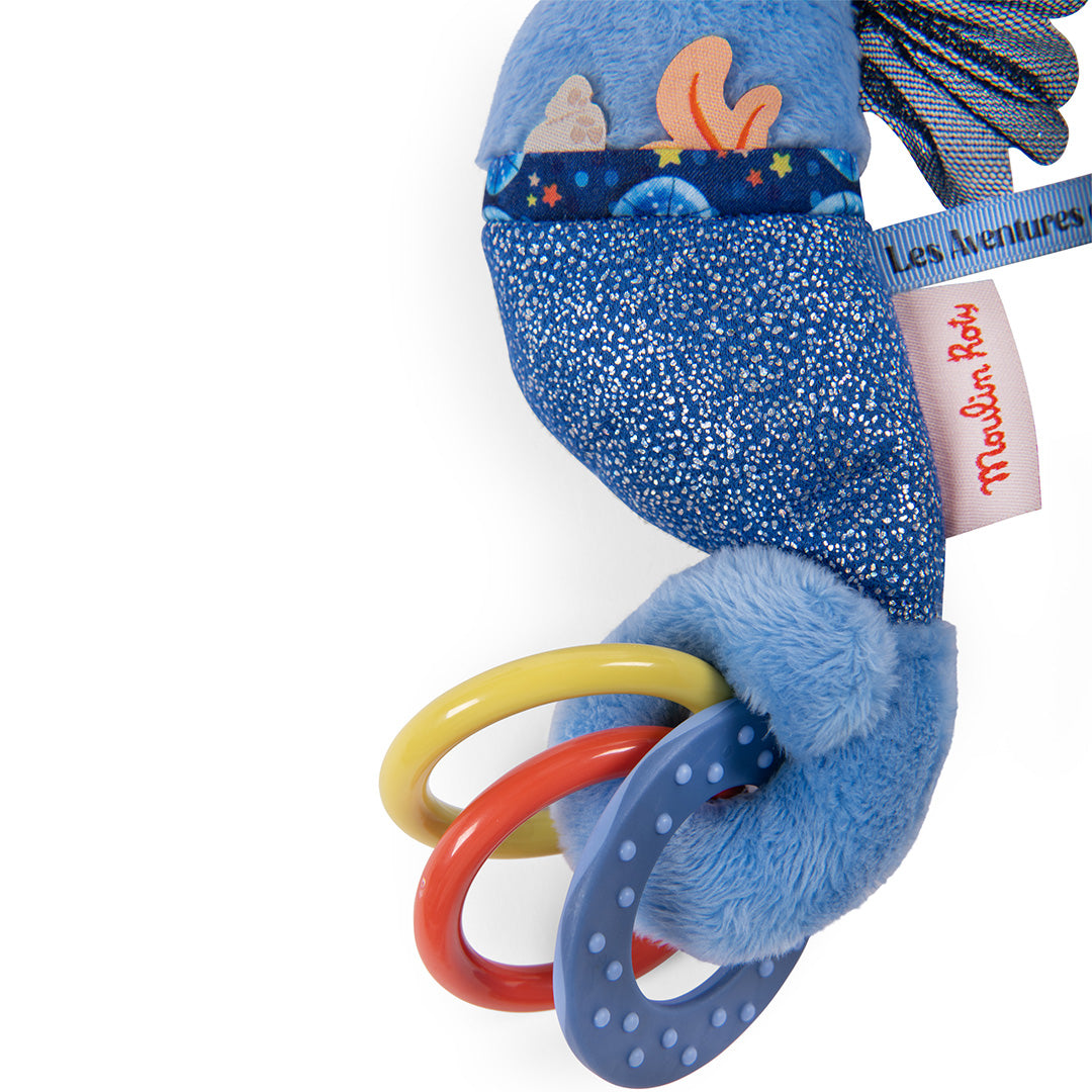 Detail van de Moulin Roty blauwe zeepaardje activiteitenknuffel met kleurrijke rammelringen en merklabel.