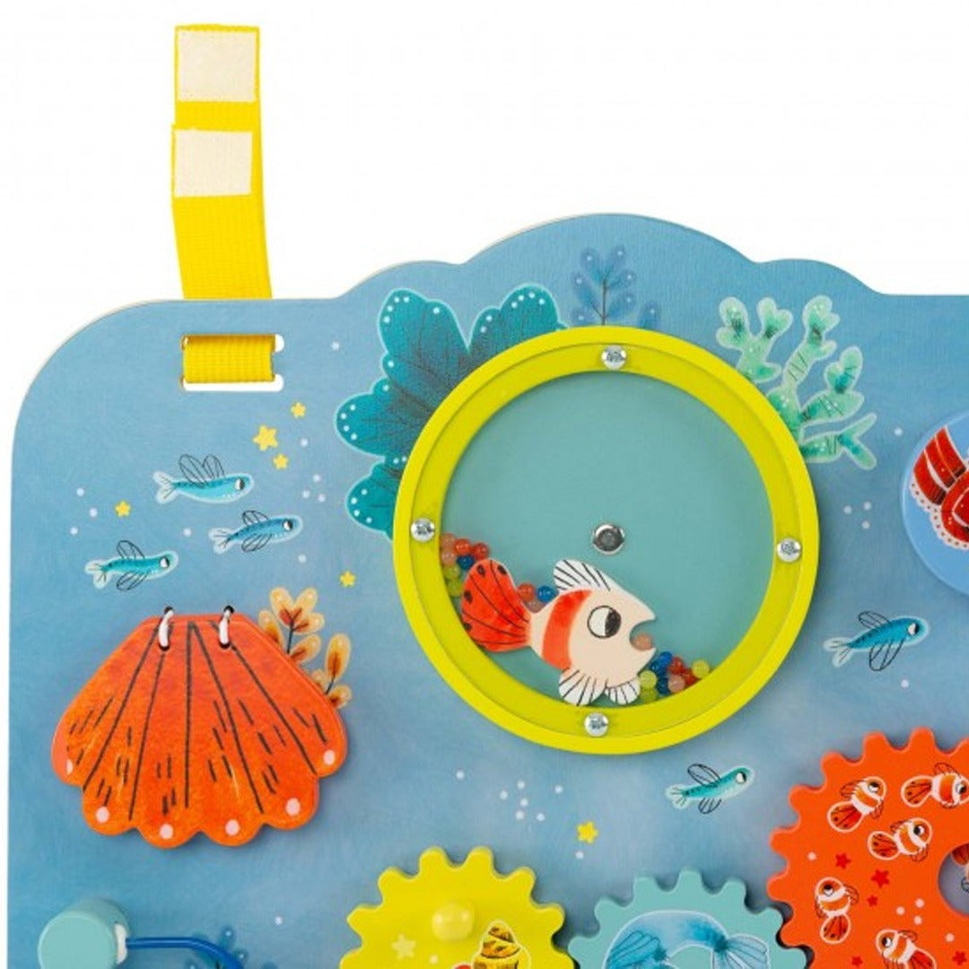 Detail van het Moulin Roty activiteitenpaneel met een gele rammelaar met vis en een oranje schelp.