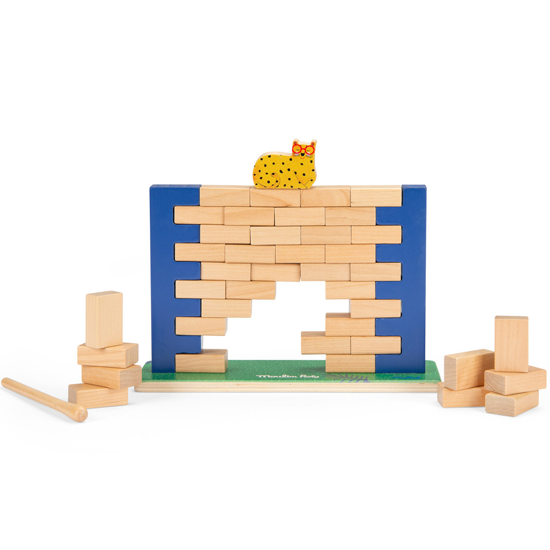 Moulin Roty balansspel met een wiebelende wand van houten bakstenen, een gele kat bovenop en losse blokken en een hamer op de grond.