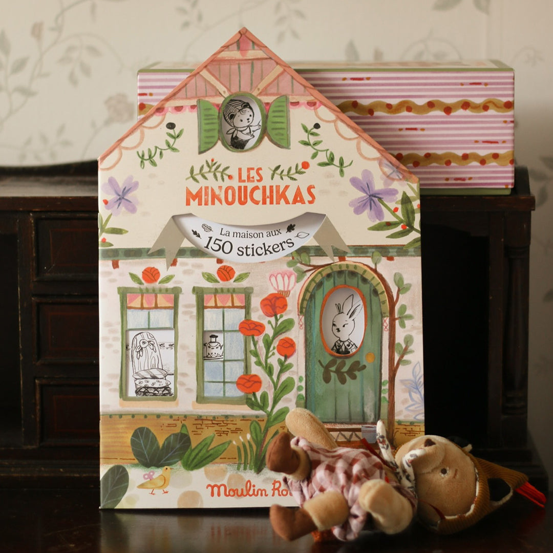 Het Moulin Roty kleur- en stickerboek Les Minouchkas staat rechtop met een knuffel ervoor.