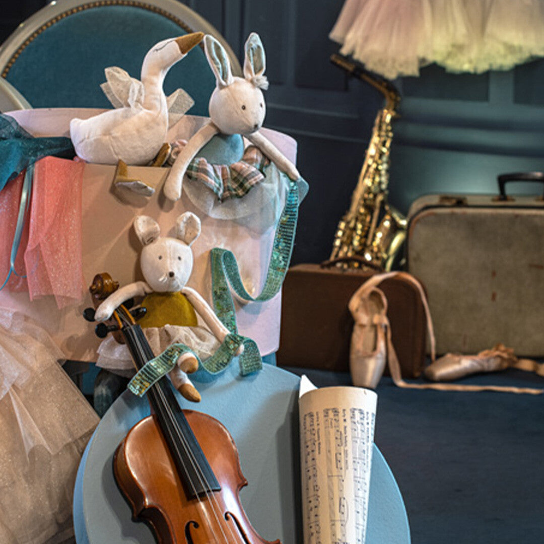 Moulin Roty knuffelkonijn en andere pluchen dieren in een theaterdecor met muziekinstrumenten en balletschoenen.